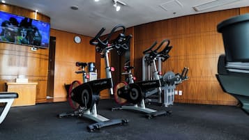 A gym with stationary bikes and a television displaying sports.