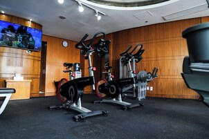 A gym with stationary bikes and a television displaying sports.