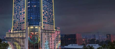 A multi-story hotel with a distinctive corner design, featuring a large glass facade and illuminated signage.