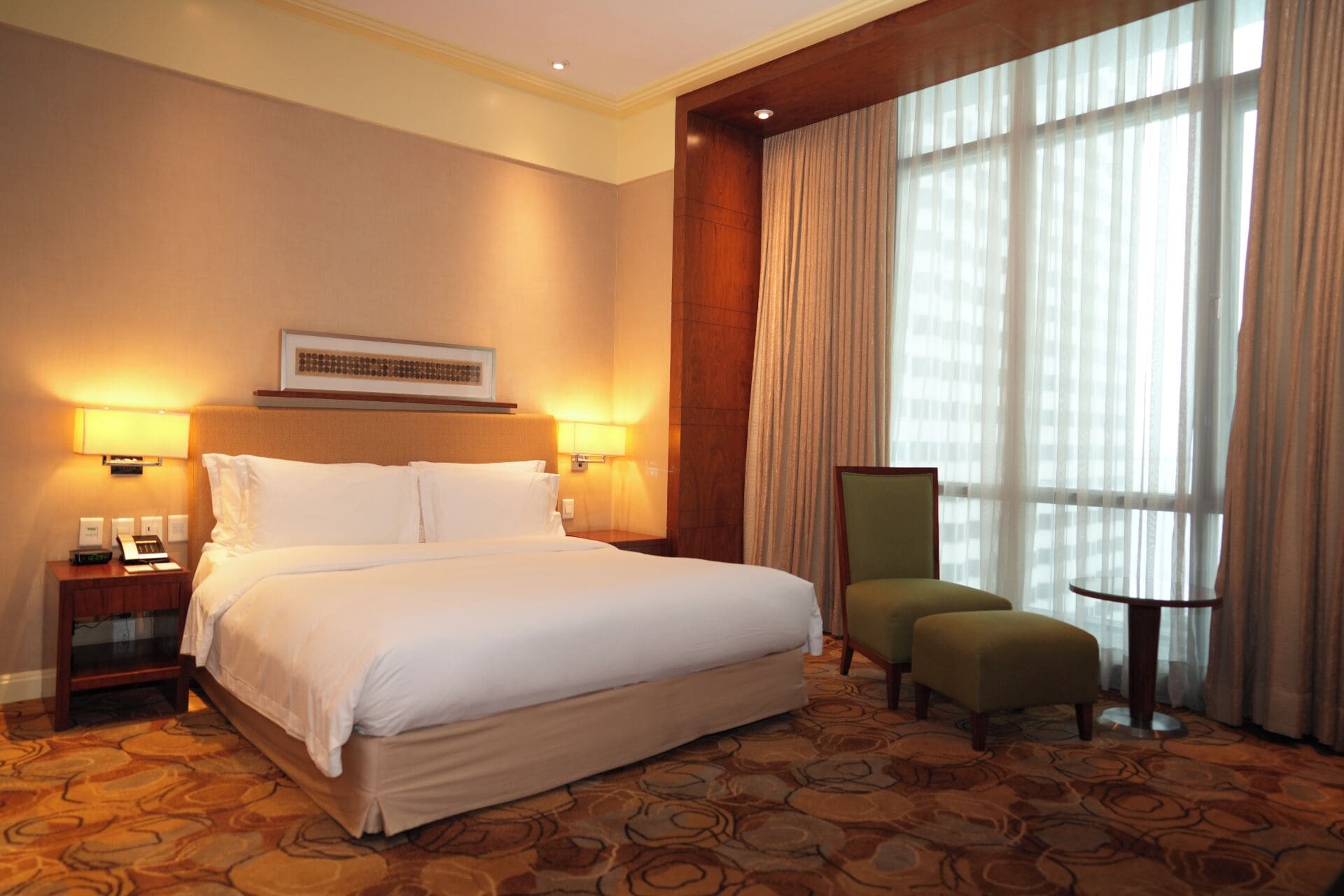 A hotel room with a large bed, two bedside lamps, a chair, and a small table.