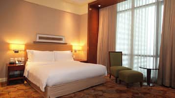 A hotel room with a large bed, two bedside lamps, a chair, and a small table.