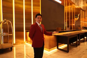 A man in a red suit standing in a hotel lobby with a reception desk and a seating area. - New Coast Hotel Manila (Manila)