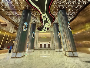 A modern lobby with a central staircase, marble flooring, and decorative lighting.