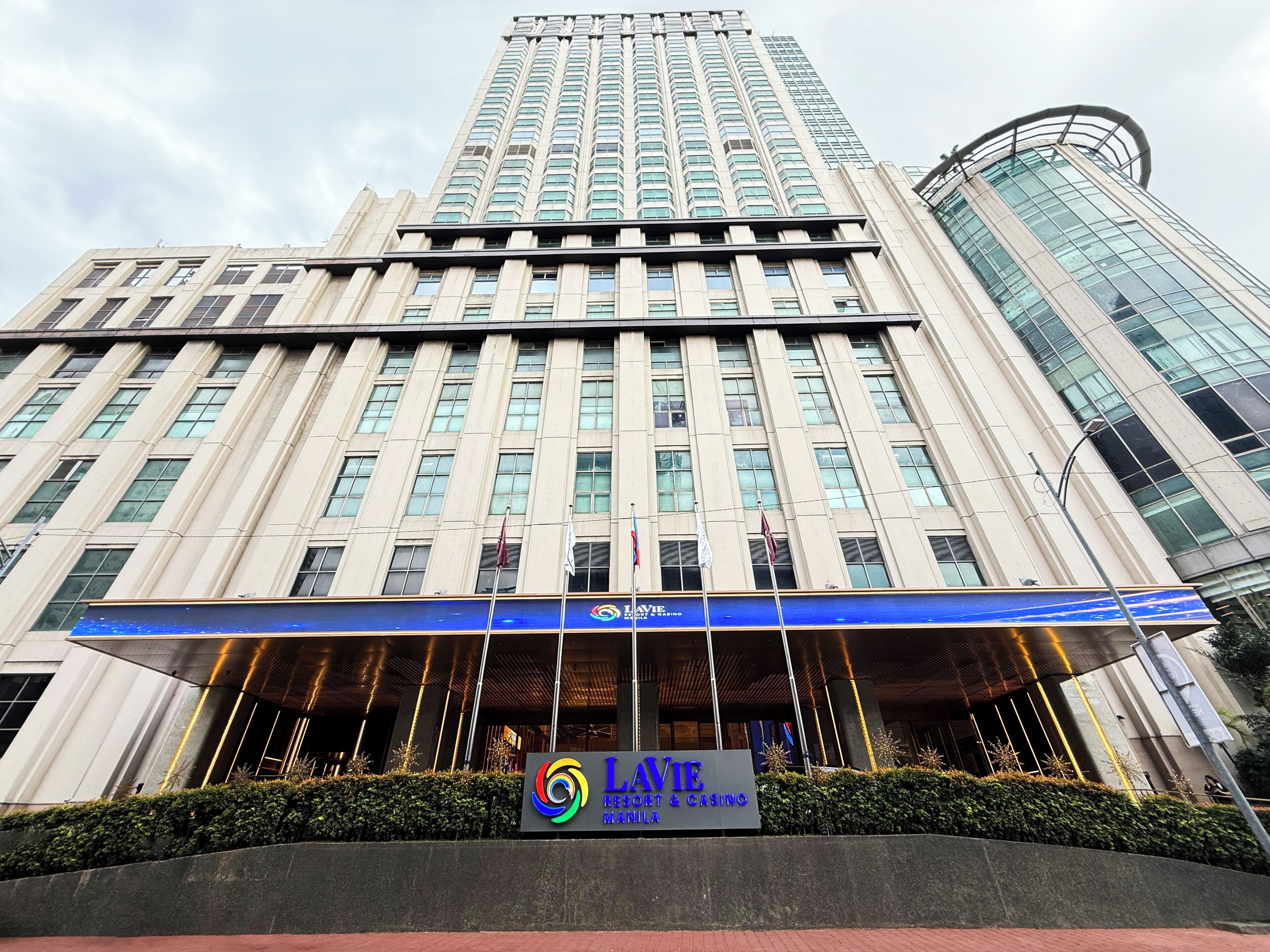 Un immeuble à plusieurs étages doté d’une entrée imposante, avec un auvent bleu et une enseigne indiquant « LAVIE Resort & Casino Manila ».