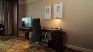 A hotel room with a desk, chair, television, lamp, and two framed pictures on the wall.