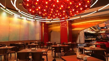 A modern restaurant interior with multiple dining tables and chairs, a distinctive red and orange color scheme, and a unique spherical light fixture.