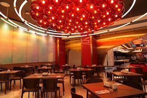 A modern restaurant interior with multiple dining tables and chairs, a distinctive red and orange color scheme, and a unique spherical light fixture.