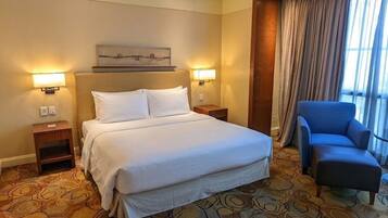 A hotel room with a large bed, two bedside lamps, a blue armchair, and a patterned carpet.