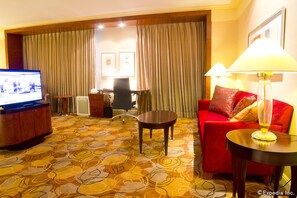 A hotel room with a red sofa, a wooden coffee table, a TV, and a desk with a chair. - New Coast Hotel Manila (Manila)