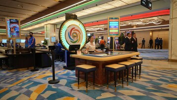 A casino gaming area with a roulette wheel, slot machines, and a bar area with stools.