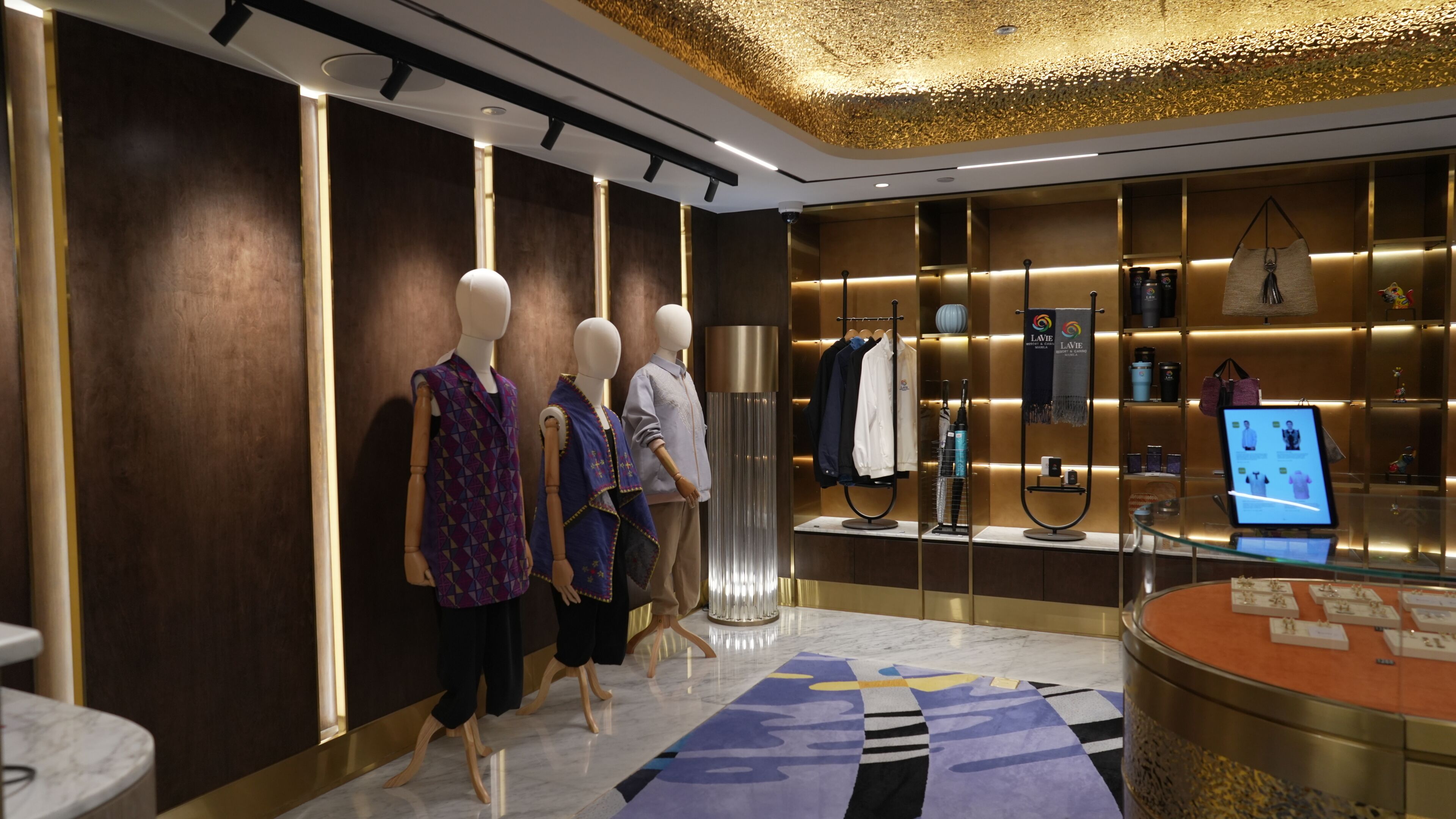 A modern hotel lobby with mannequins displaying clothing, a digital information kiosk, and a patterned carpet.