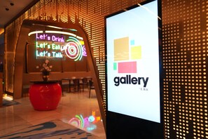 Een hotel lobby met een neonbord waarop staat 'Let's Drink, Let's Eat, Let's Talk' en een groot scherm dat het woord 'gallery' toont, inclusief een logo.