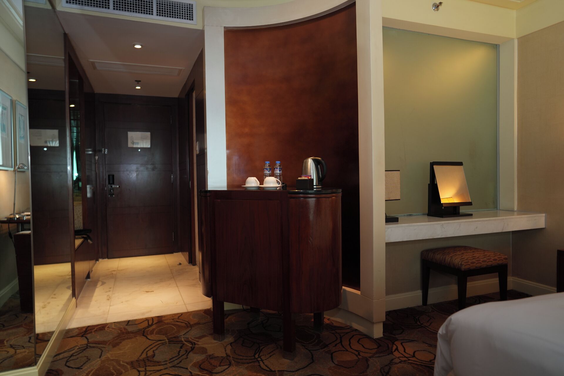 A hotel room with a desk, a chair, a bed, and a small table with a kettle and cups.