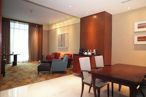 A hotel room with a dining area, a sofa, a coffee table, and a large wooden accent wall.