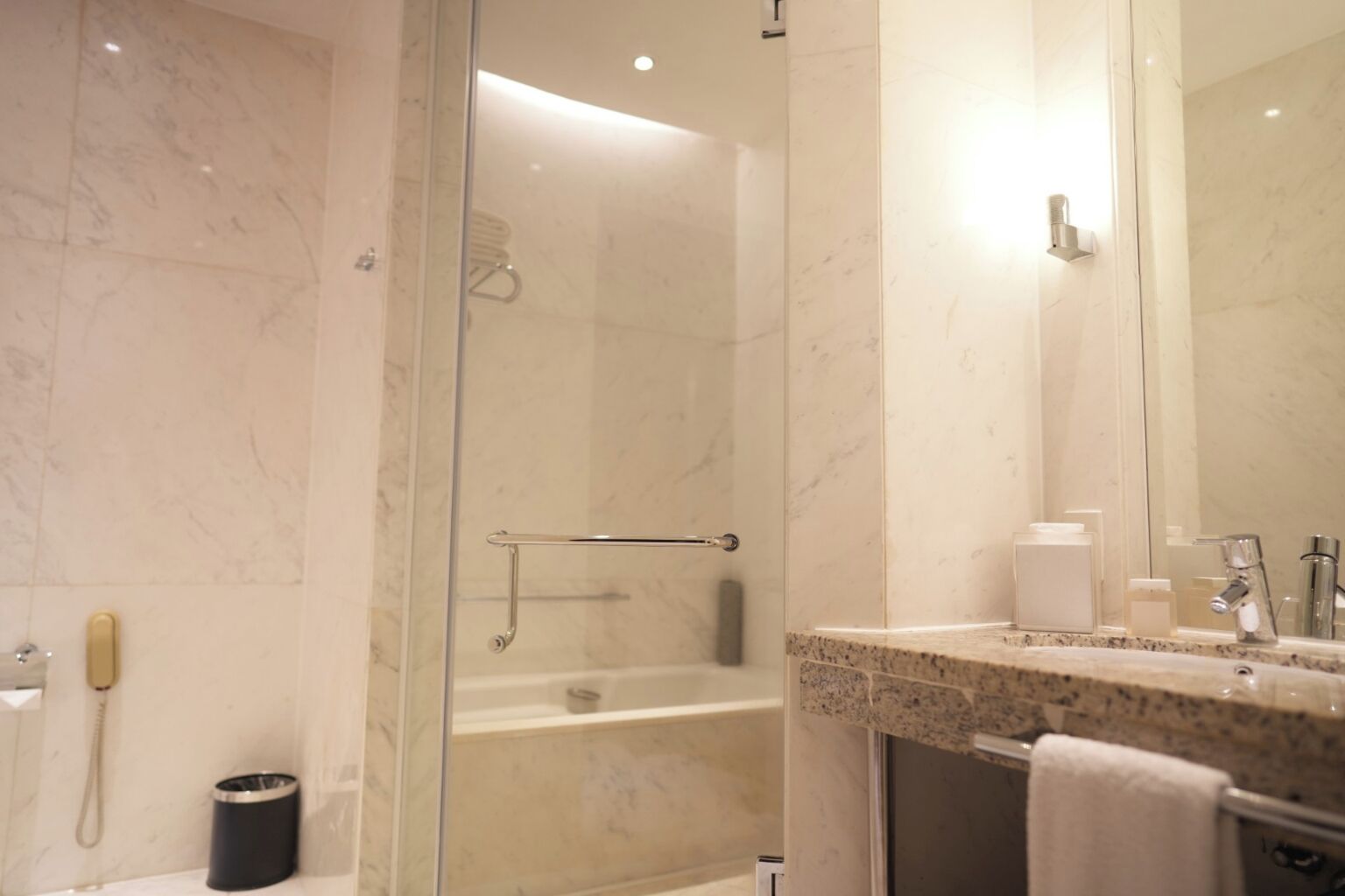 A modern bathroom with a glass-enclosed shower, a marble-tiled wall, a sink with a mirror, and a towel rack.