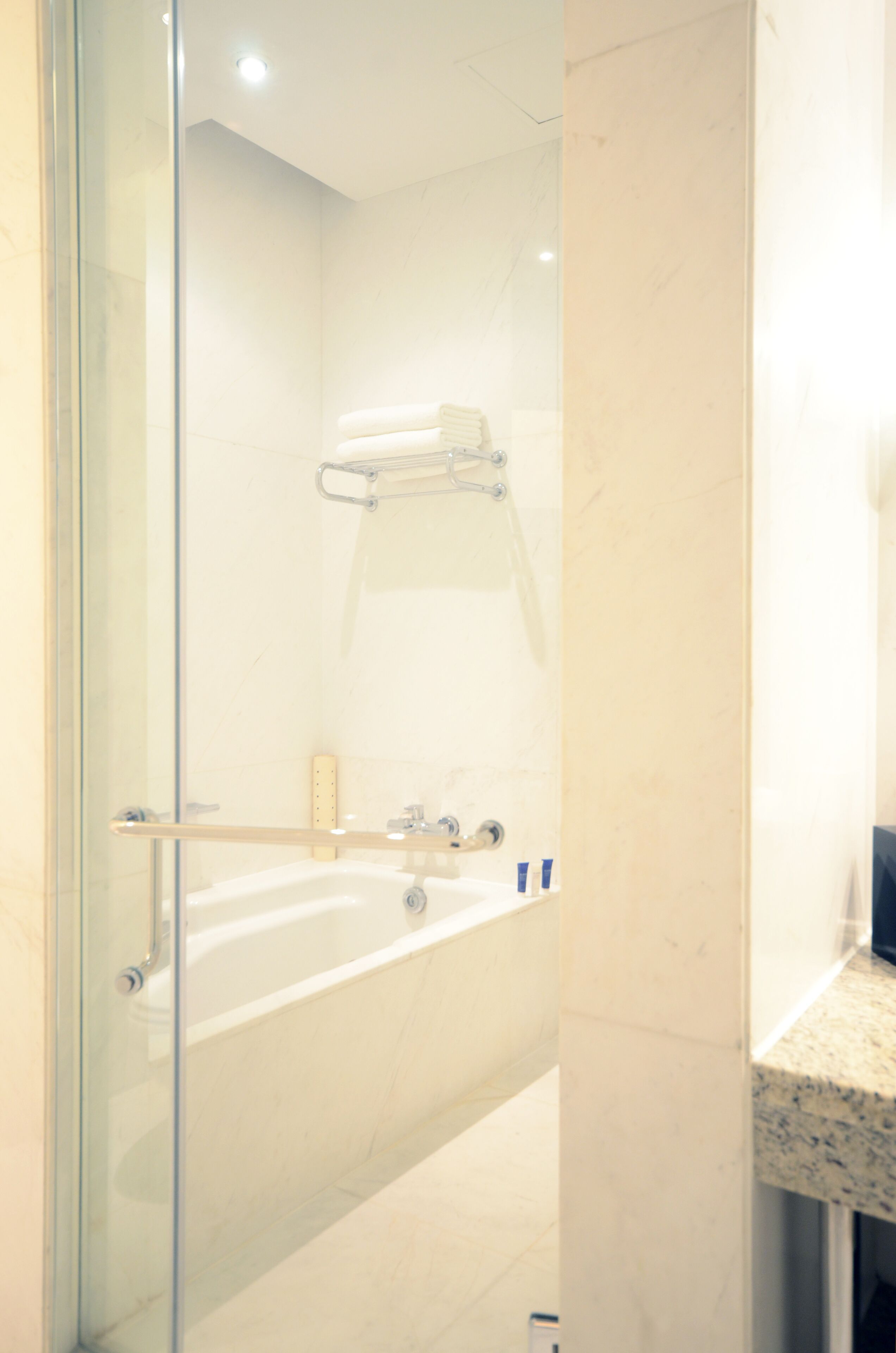 A modern bathroom with a glass shower enclosure, a white bathtub, and a marble countertop.
