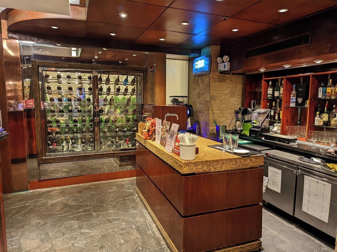A bar area with a counter, shelves with bottles, and a television screen.