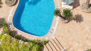 Un área de piscina en la azotea con dos piscinas, rodeada de palmeras y sillas de descanso blancas.