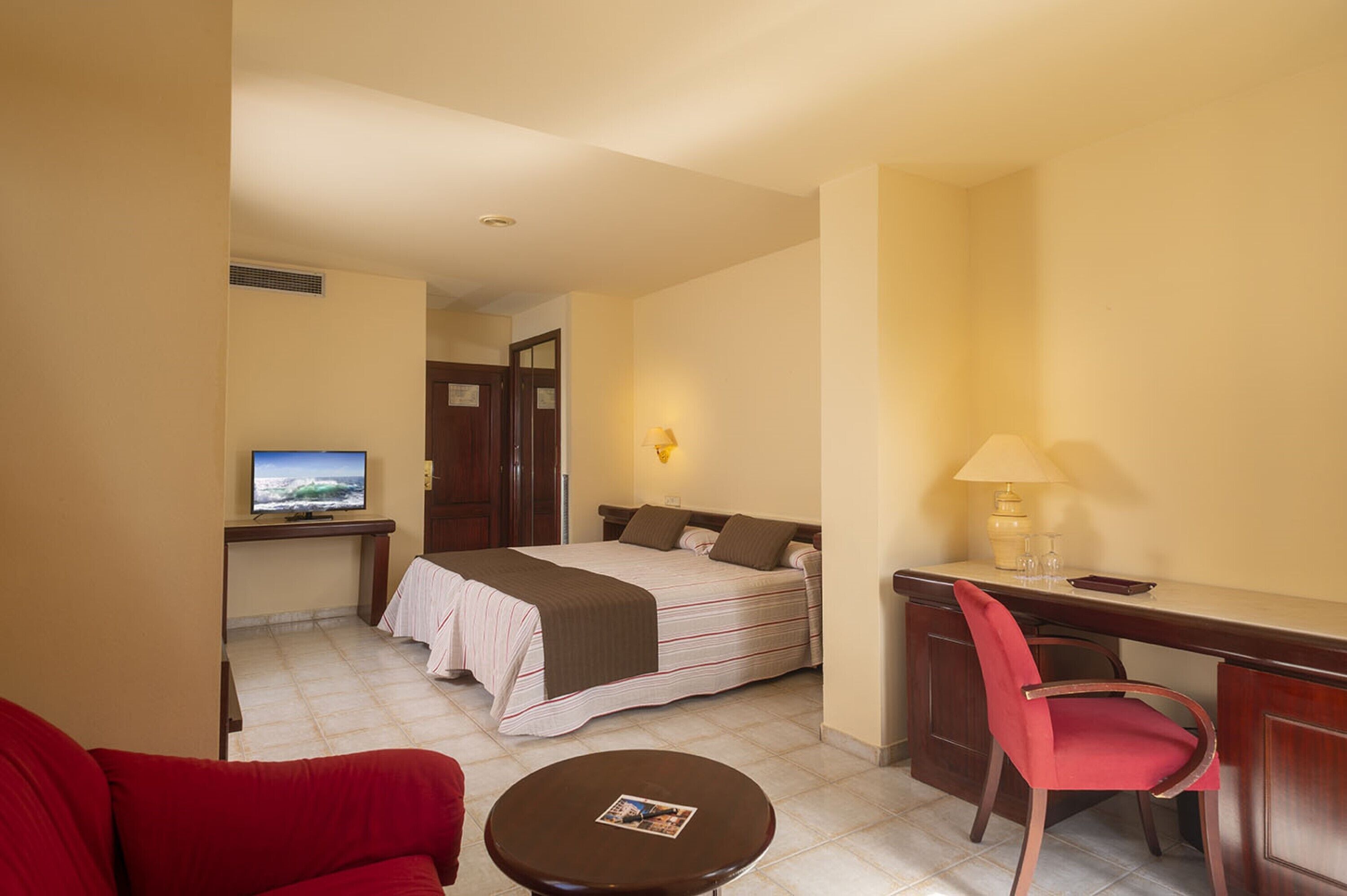 Une chambre d’hôtel comprenant un lit, un bureau avec une chaise, une télévision et une petite table avec une lampe.