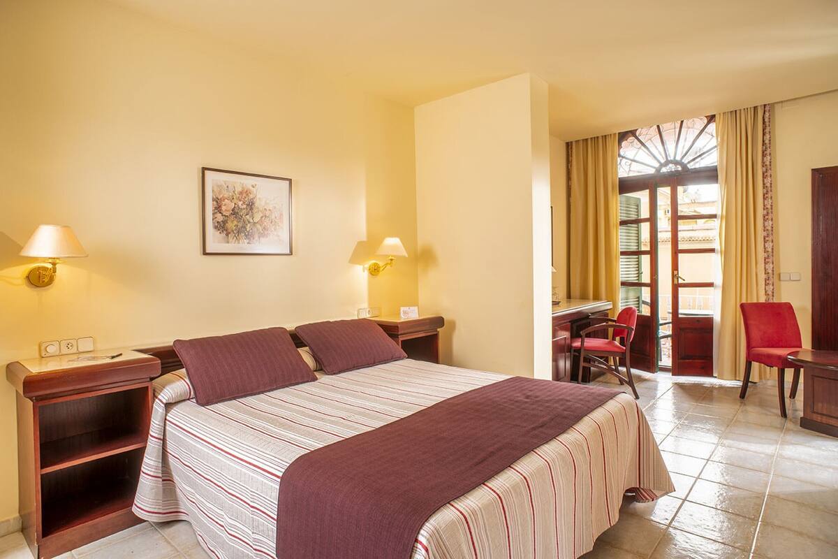 A hotel room with a bed, bedside tables, lamps, a desk, a chair, and a window with curtains.
