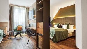 Una habitación de hotel moderna con piso de madera, un sillón verde, un escritorio con una silla, una cama con una colcha verde y un ventanal con cortinas.
