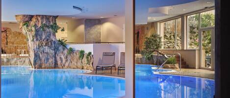 An indoor swimming pool with a rock wall, lounge chairs, and a view of the outdoors.