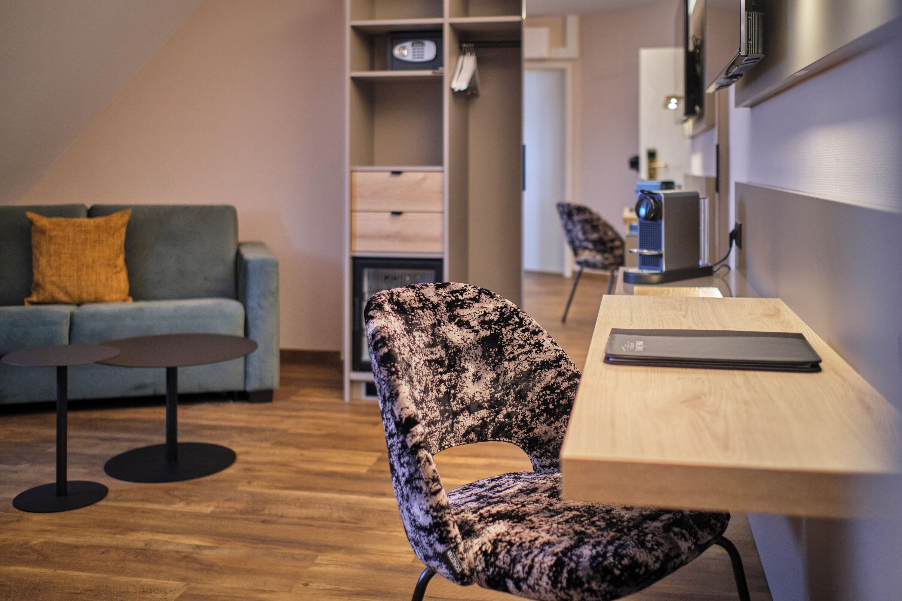 A modern room with a sofa, a patterned chair, a small table, and a desk with a laptop.
