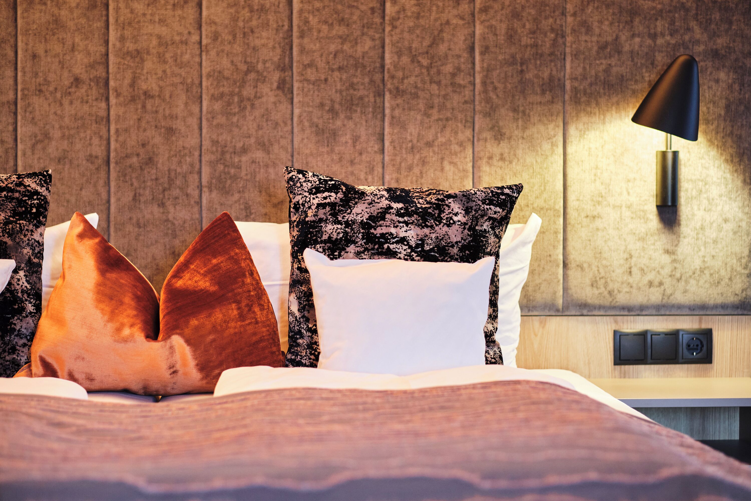 Un lit bien fait, agrémenté d’oreillers à motifs et d’une lampe murale au design moderne.