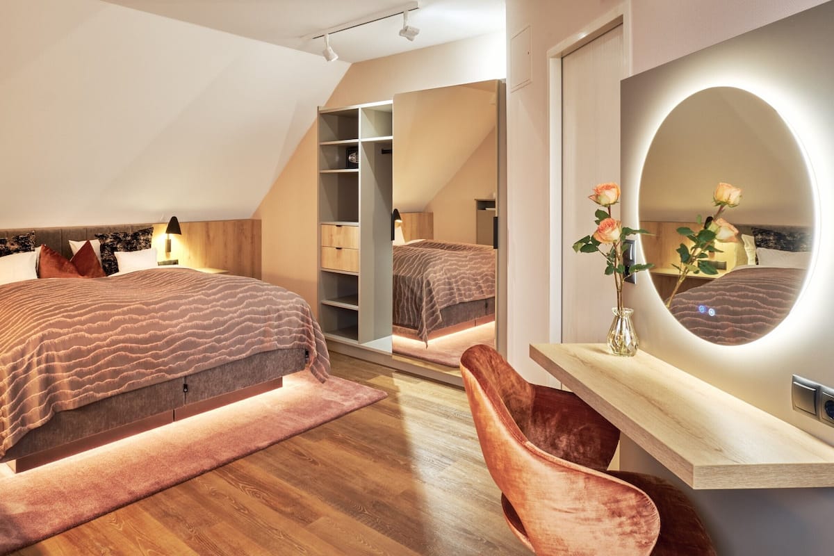Een moderne slaapkamer met een groot bed, nachtkastjes, een kaptafel met spiegel en een inloopkast.