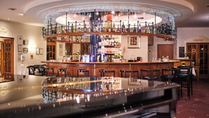 Una zona de bar con diversas opciones de asientos, una barra central y un techo decorado con luces colgantes.