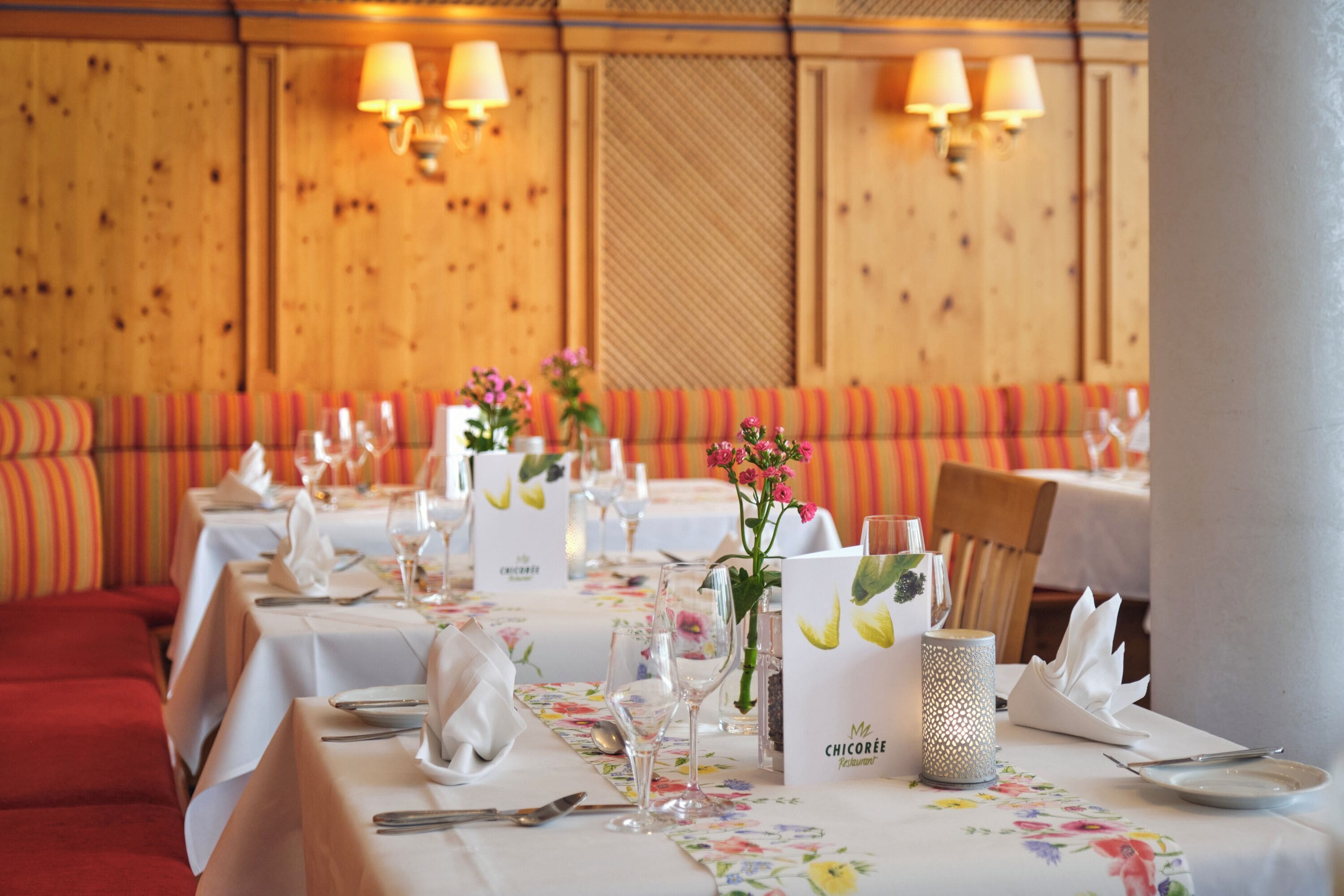 A restaurant with tables set for dining, featuring floral tablecloths and neatly arranged table settings.