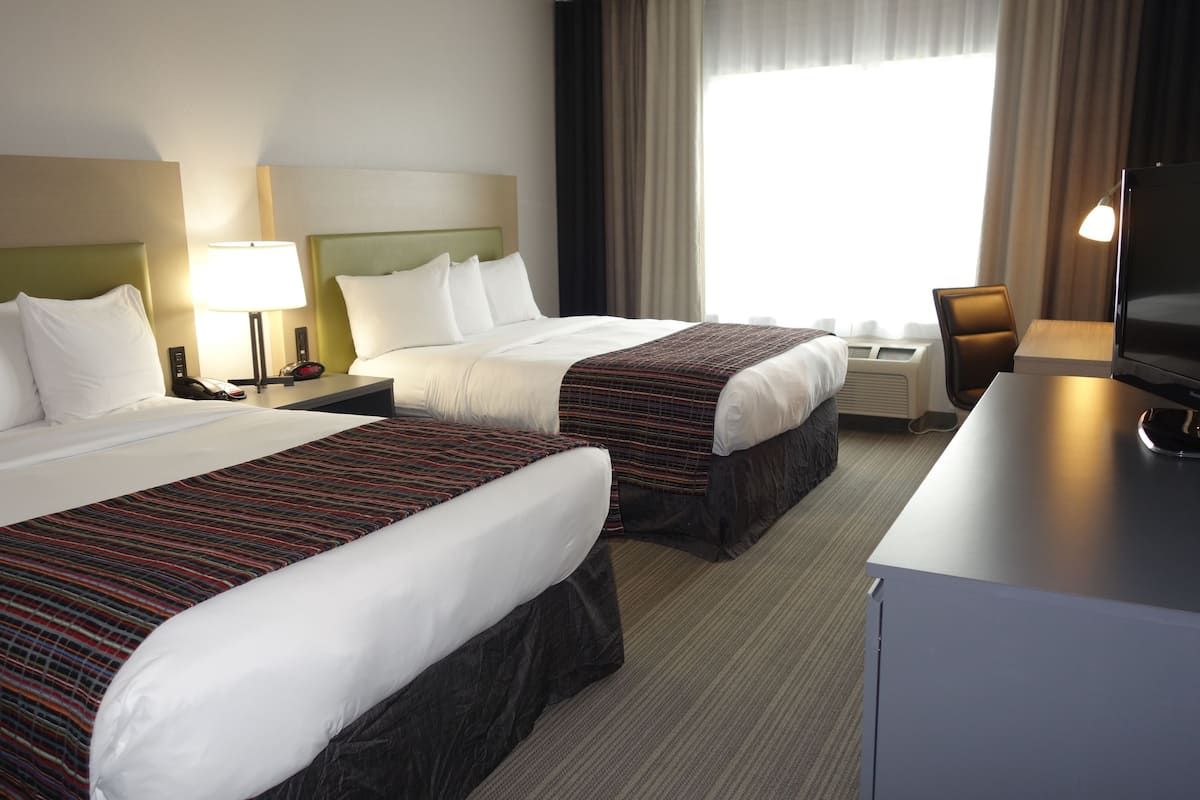 A hotel room with two beds, a desk, a chair, a television, and a window with curtains.
