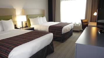 A hotel room with two beds, a desk, a chair, a television, and a window with curtains.