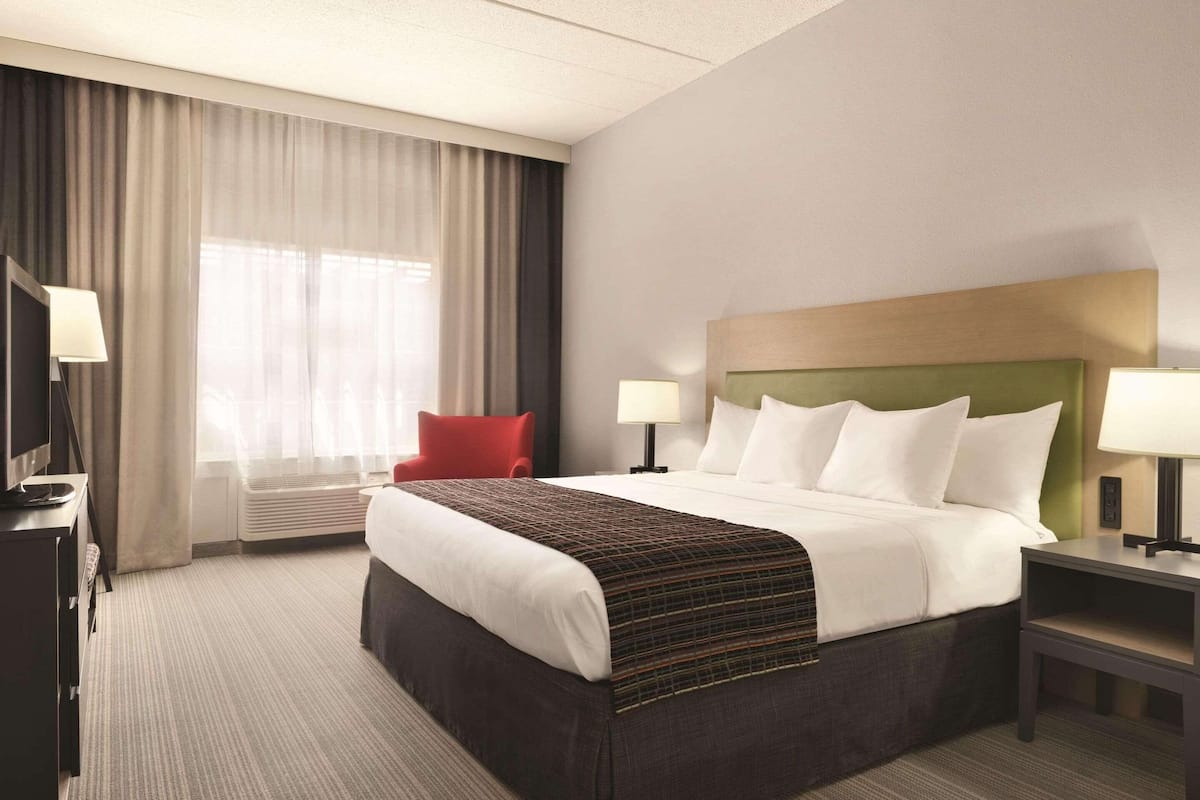 A hotel room with a large bed, two bedside tables with lamps, a red chair, and a television.