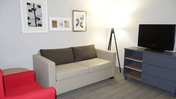 A modern living room with a sofa, a red chair, a TV on a stand, and framed artwork on the wall.