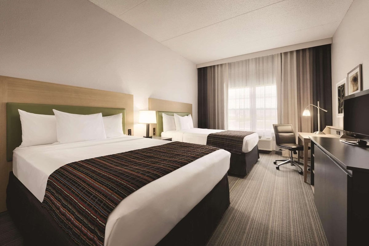 A hotel room with two beds, a desk, a chair, and a television.