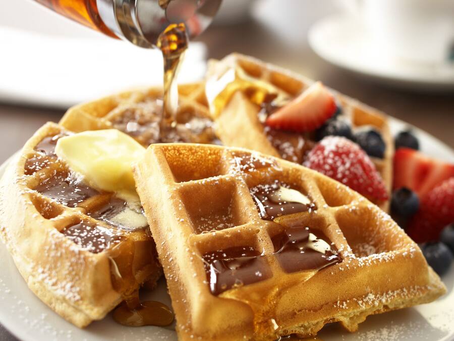 Ein Teller Waffeln mit Sirup und Obst.