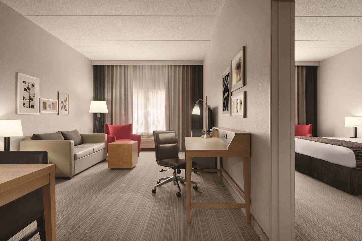 A hotel room with a sofa, a desk, a chair, a bed, and a window with curtains.