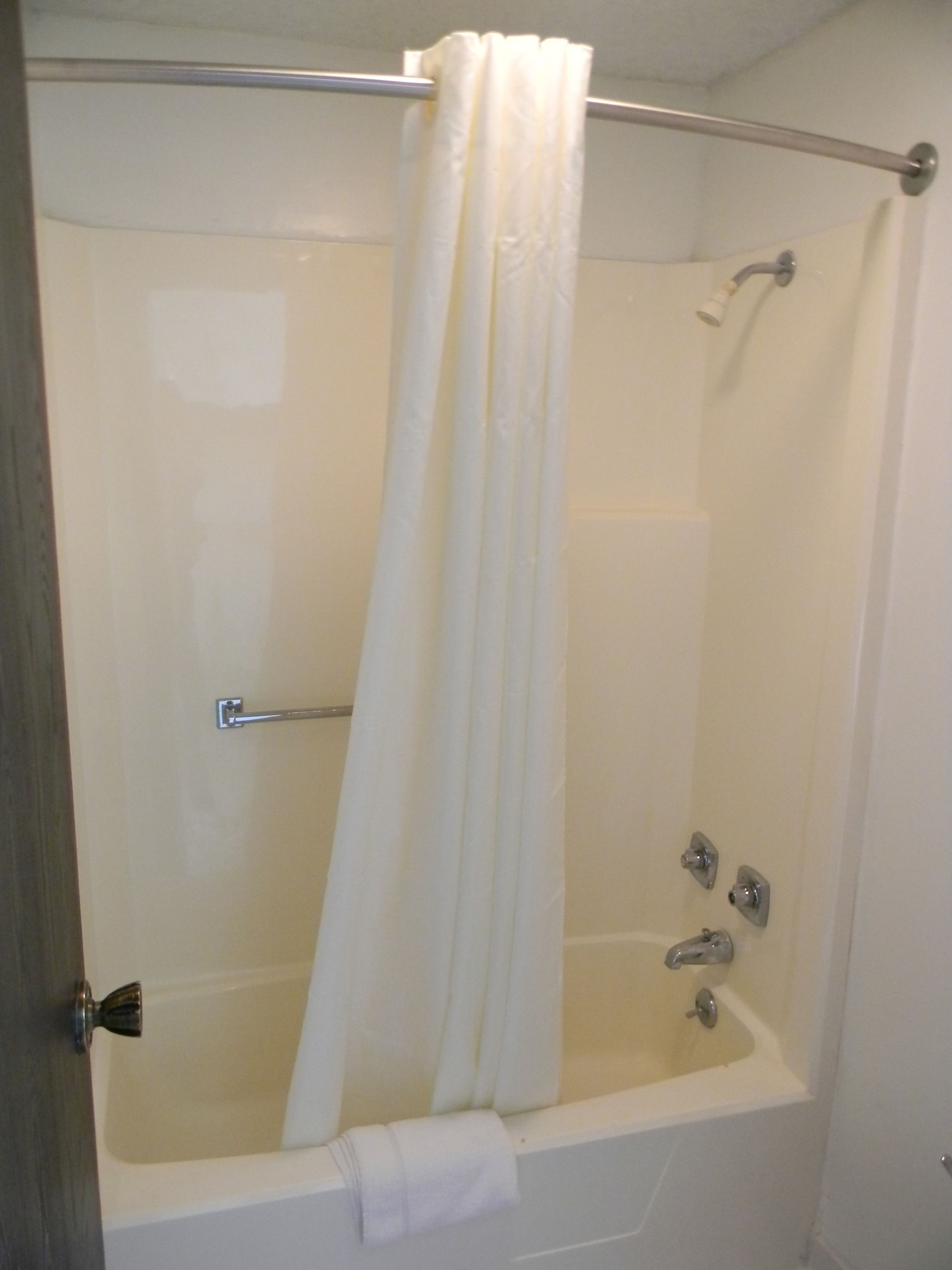 A shower with a white curtain, a grab bar, and a handheld showerhead.