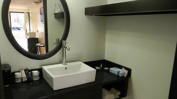 A bathroom with a white sink, black countertop, and a round mirror. There is a towel rack with towels and a soap dispenser on the countertop.