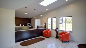 A reception area with a counter, two orange chairs, a large window with a view, and a skylight. - Americas Best Value Inn Heath Newark (Heath)