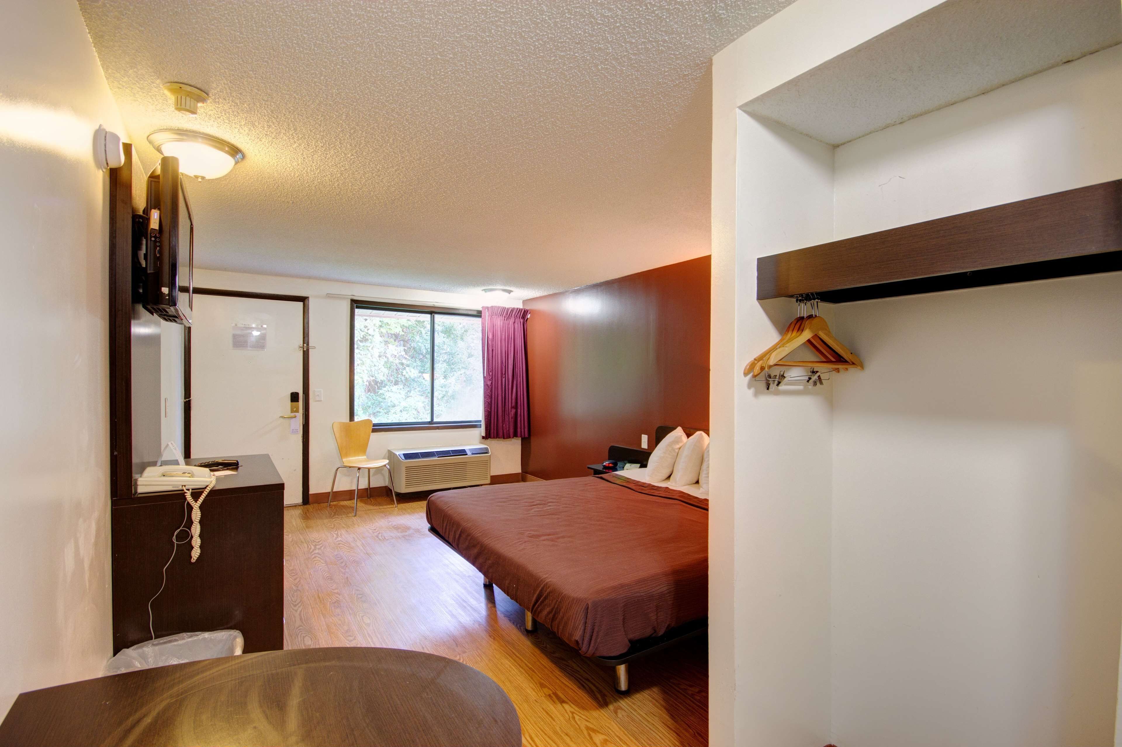 Habitación de hotel con cama, escritorio con teléfono, silla, ventana con cortinas y perchero.