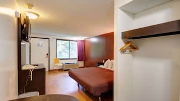 Habitación de hotel con cama, escritorio con teléfono, silla, ventana con cortinas y perchero.