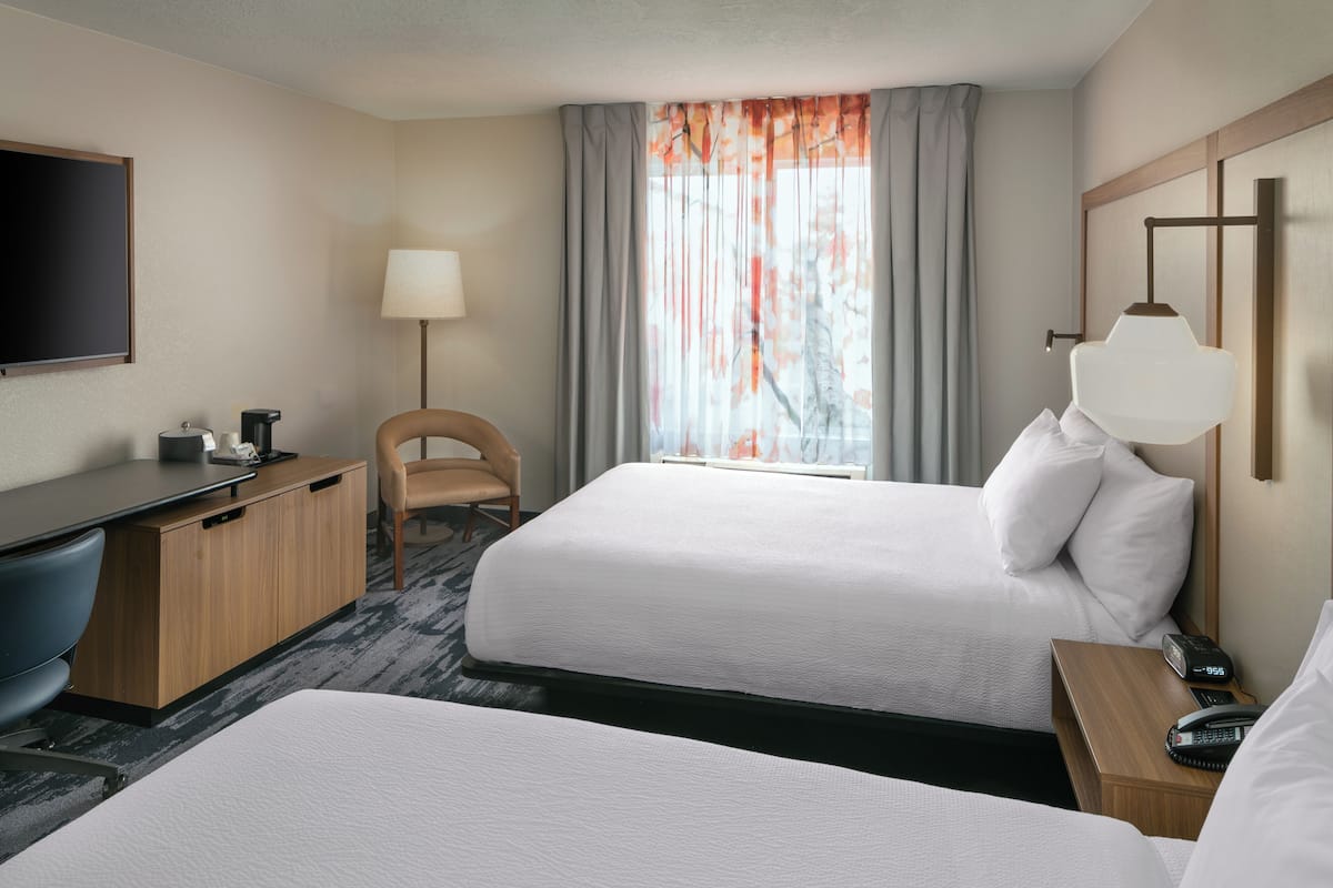 A hotel room with two beds, a desk, a chair, a TV, and a window with curtains.