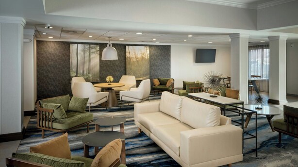 A spacious living area with a large sofa, armchairs, a coffee table, and a dining table. There is a large window with a view of trees, and the room has a modern design with a patterned carpet. - Fairfield Inn and Suites by Marriott Anchorage (Anchorage)