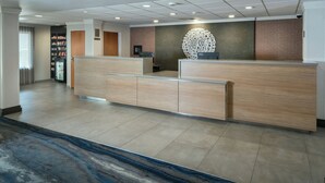 A reception area with a wooden reception desk, a large decorative wall piece, and a refrigerator with snacks. - Fairfield Inn and Suites by Marriott Anchorage (Anchorage)