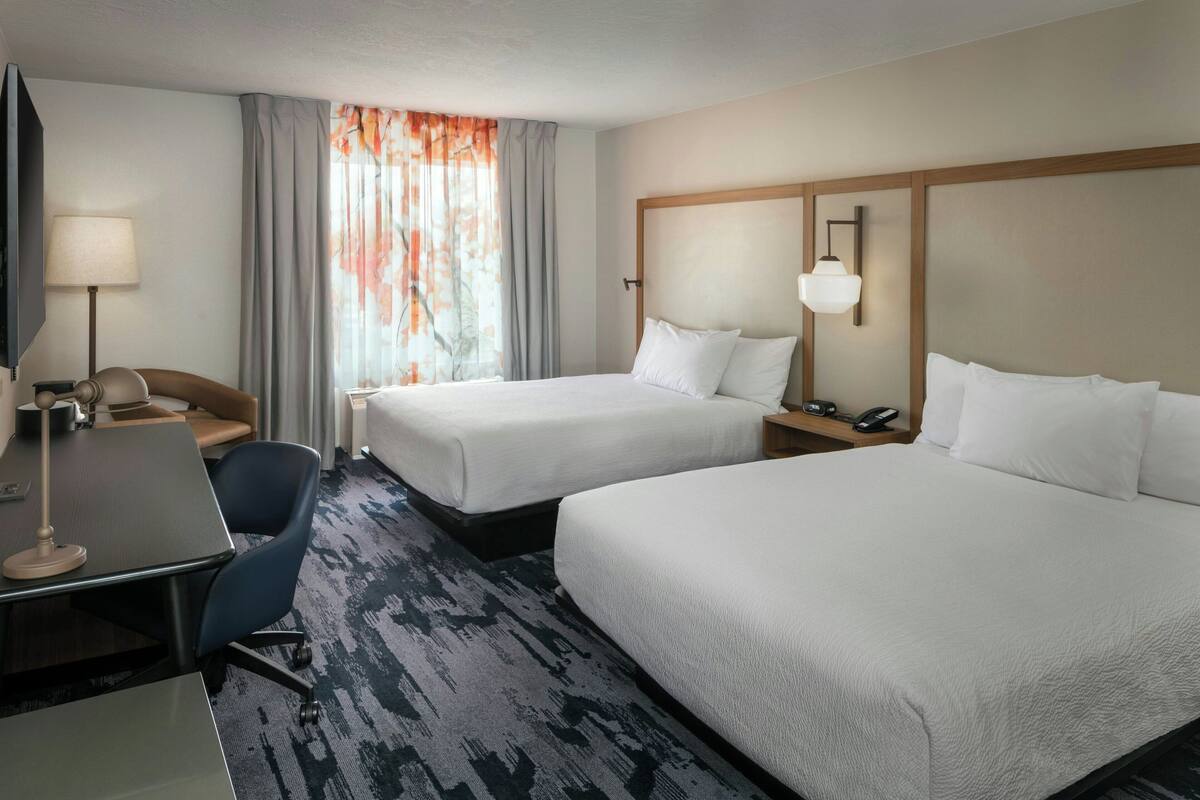 Une chambre d’hôtel avec deux lits, un bureau avec une chaise, une télévision et une lampe.
