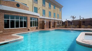 A swimming pool area with a brick building, large windows, and a clear sky.