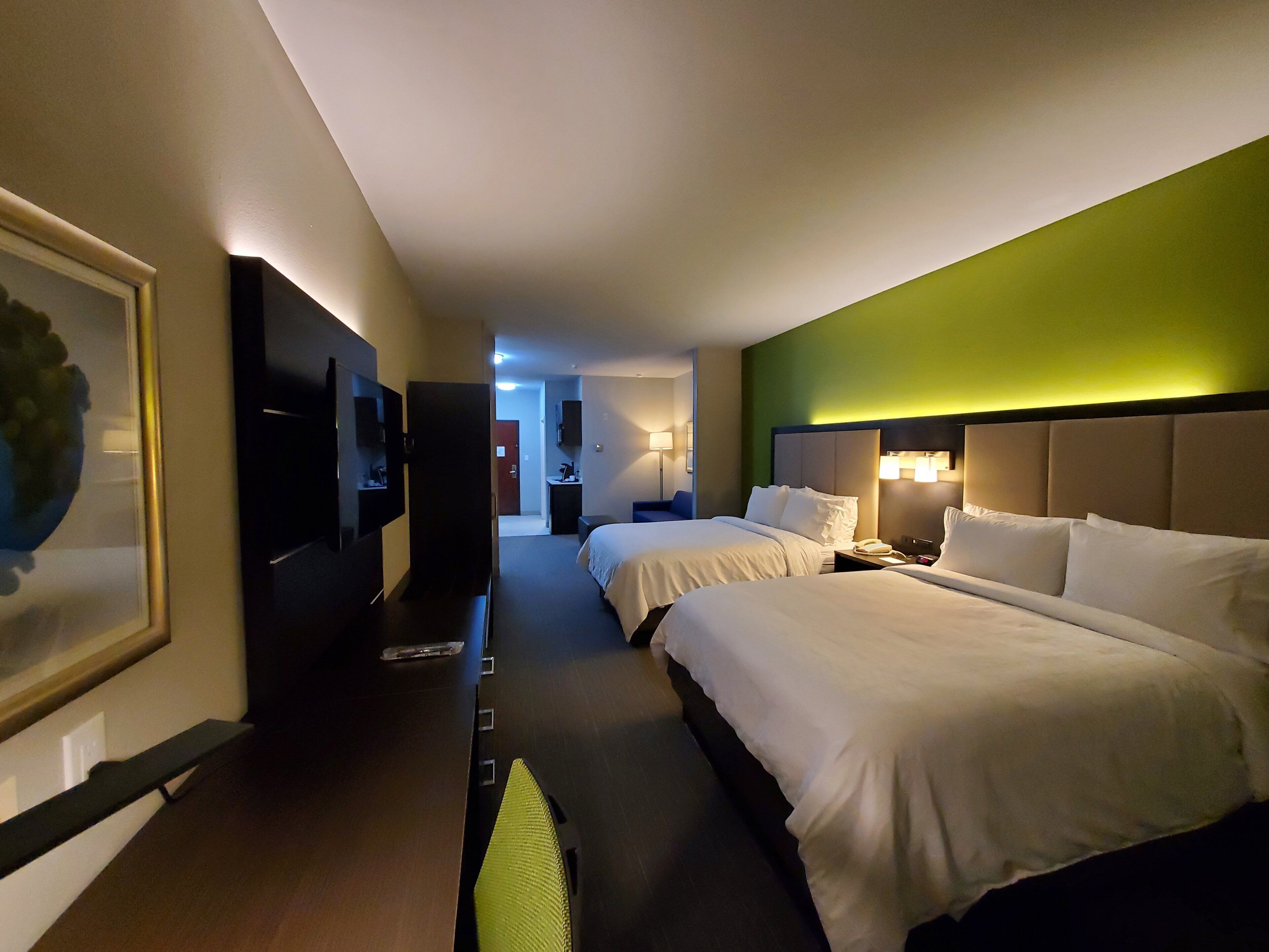 A hotel room with two beds, a TV, a desk, and a green accent wall.