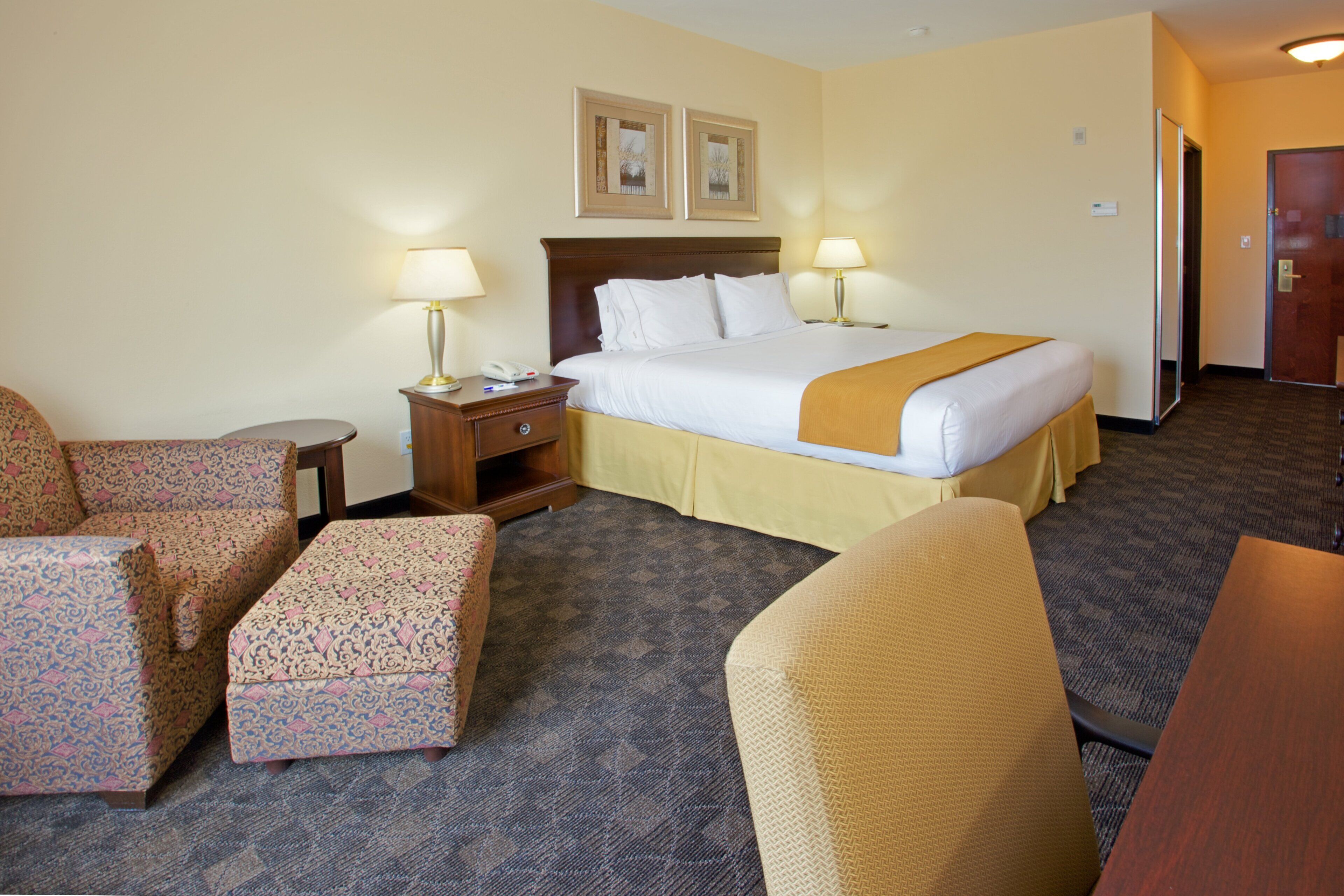 A hotel room with a bed, two bedside tables with lamps, a chair, a small table, and a sofa.